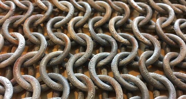 Close up of 3D printed chainmail with some paint applied to look like slight rust.