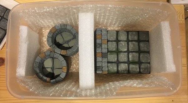 Tabletop terrain pieces stored in a plastic container surrounded by bubble wrap and foam.